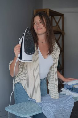 Günlük giysiler giymiş bir kadın buharlı ütüyle giysileri ütülüyor bakterileri öldürüyor ve temiz bir gardırop yaptırıyor.