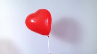 Kırmızı bir kalp şeklindeki balon, 14 Şubat kutlamasını simgeleyen beyaz bir arka planda ileri geri sallanıyor. Yüksek kalite 4k görüntü
