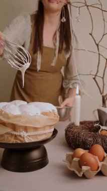 Paskalya pastasına beyaz krema döken bir kadın yanan mumlar ve yumurtalarla dolu bir masada şenlikli bir tatlı yaratıyor. Yüksek kalite 4k görüntü