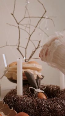 Güzel dekore edilmiş bir Paskalya masasında kadın pasta yumurtalarının yanında mum ve mumlarla süslenmiş tahta bir çelenk yakar. Yüksek kalite 4k görüntü
