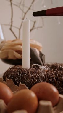 Paskalya yumurtası pastası ve dekoratif mum çelengi ile dekore edilmiş bir masanın üzerinde mum yakan bir elin yakın çekimi. Yüksek kalite 4k görüntü