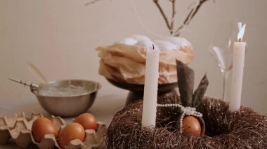 Paskalya masasında yavaşça yanan bir mumu kapat. Tepsi dekoratif çelenk ve ağaç dalında kek yumurtaları. Yüksek kalite 4k görüntü