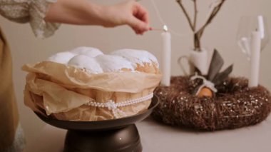 Paskalya atmosferi yaratan bir kadın kek ahşap çelengi ve süslü yumurtalarla mum yakıyor. Yüksek kalite 4k görüntü