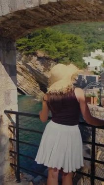 Kaya kemer kamerasının önünde dikilen kahverengi etekli ve hasır şapkalı kadın Petrovac 'taki küçük kaleyi ve kayalıkları gözler önüne seriyor. Yüksek kalite 4k görüntü