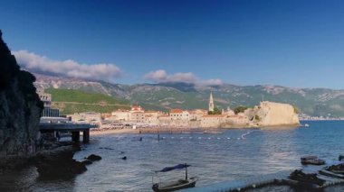 Budva kayalık turuncu kıyı manzarası. Yığılmış uçurumlar, deniz boyunca yeşil ağaçlar ve insanların plajlar arasında yürüdüğü taş patikalar. Yüksek kalite 4k görüntü