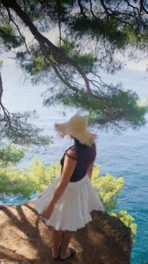 Yazlık etek ve hasır şapkalı kız uçurumun kenarında dans ediyor ve Adriyatik Denizi 'nin kaya dalgaları ile yeşil Karadağ tepelerinin üzerinden uçuyor. Yüksek kalite 4k görüntü