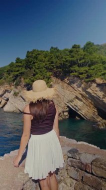 Uçurumun kenarındaki beyaz etekli, yeşil uçurumlar sallayan ve Adriyatik 'te dramatik bir manzara dalgalandıran yaz kıyafetli bir kadın. Yüksek kalite 4k görüntü