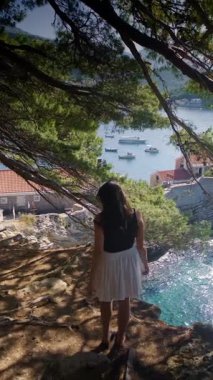 Açık etekli bir kız Petrovac Riviera 'nın yeşil tepeleri ve açık mavi Adriyatik Denizi' nin panoramik manzarasıyla uçurumun kenarında yürüyor. Yüksek kalite 4k görüntü