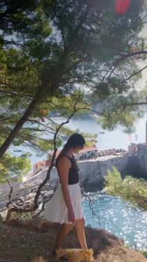 Petrovac Riviera Karadağ 'ın kayalık yeşil tepeleri ve mavi deniziyle yaz kıyafetli bir kız uçurumun kenarından manzaranın keyfini çıkarıyor. Yüksek kalite 4k görüntü