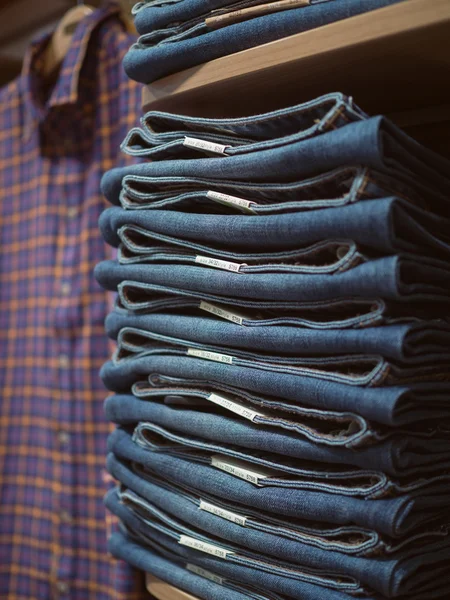 Clothing store. Folded jeans on shelf in background of checkered — Stock Photo, Image