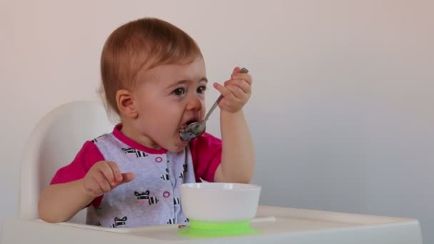 Niña come gachas se sienta en una silla — Vídeos de Stock