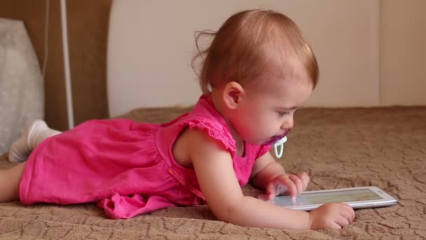 Маленька дитина лежить на дивані і грає з планшетом — стокове відео