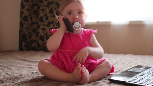 Small kid plays with smartphone sitting on couch near window — Stock Video