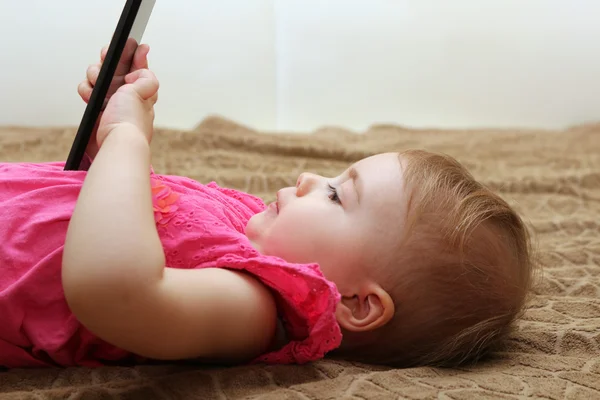 Pequeña linda chica acostada en el sofá y jugando con un teléfono inteligente — Foto de Stock
