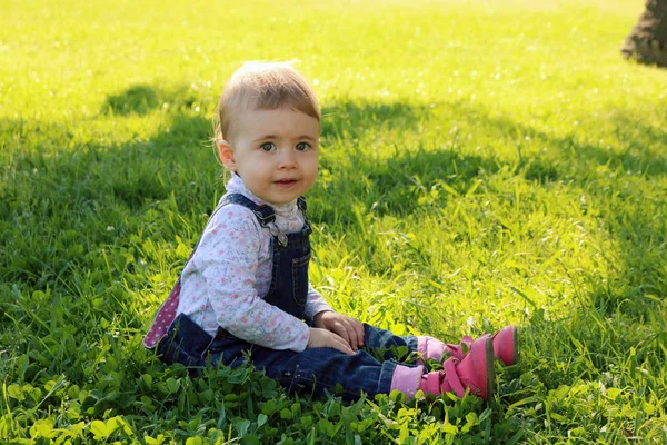 Precioso bebé sentado en la hierba verde en el parque y sonriendo para los días felices de verano — Foto de Stock