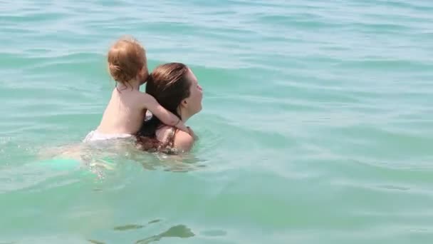 Joven madre feliz con una niña pequeña en la espalda. Familia feliz nadando en verano Al aire libre . — Vídeos de Stock