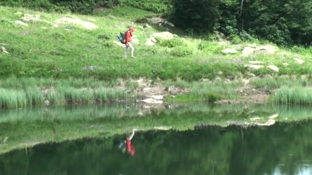 산속에 호수를 따라 걷는 배낭 등산객과 여자. 호수에 반영 하는 여자 — 비디오