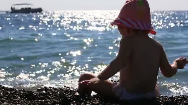 Pequeno bebê no panamá brincando na praia em um fundo de mar azul e barcos à vela. Full HD. 1920x1080 — Vídeo de Stock