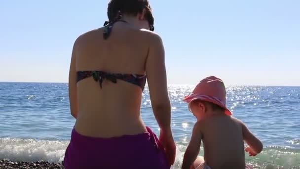 Glückliche junge Mutter, die mit ihrem Kind am Strand vor blauem Meer spielt. Voll hd. 1920x1080 — Stockvideo