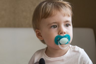 Bebek yatak odasında oturup ağzında kukla ile