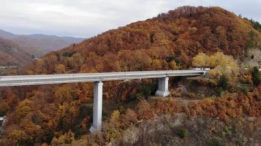 Dağlardaki Beton Sütunlar üzerindeki Otoyol Viyadük 'ünün havadan görünüşü. Dağ köyü yakınlarındaki yeşil vadideki Autobahn üzerinde uçuş. Köprü yolunda trafik var. Araçların üzerinden uç. 4k