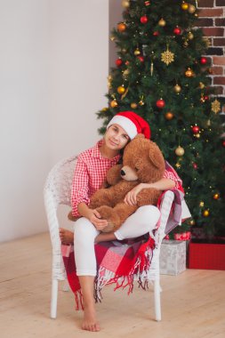 tatil, hediyeler, Noel, çocukluk ve insan kavramı - oyuncak ayı ile santa yardımcı şapkalı kız ışık arka plan üzerinde gülümsüyor.