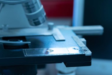 Bir optik mikroskop rafında analiz edilecek bir numuneyle birlikte slayt, aseptik laboratuvar ortamından mavi atmosfer, araştırma ve geliştirme kavramı