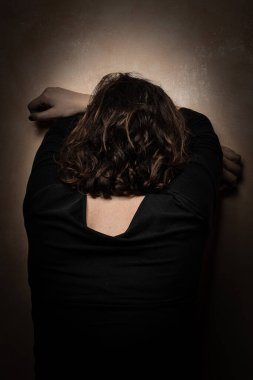 Yalnız ve terk edilmiş bir kadın, alnını duvara dayayıp umutsuzluğa kapılmış, karanlık ve kasvetli bir atmosferde geri dönmüş. Kadın hayal kırıklığı ve depresyonu kavramı