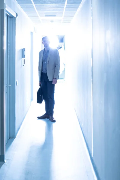 Silhouette of doctor along a hospital ward with his own briefcase, backlit lighting and cool light tone