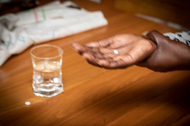 Blurry closeup of an African lady's shaking hands with pills and a glass of water. Concept of Parkinson's disease related problems due to tremor cure drugs.