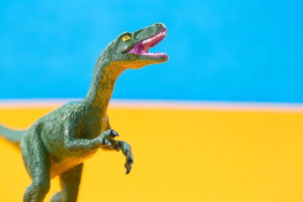 зеленый сердитый динозавр игрушка на синем и желтом фоне 