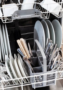 Bulaşık makinesi beyaz bulaşıklar ve gümüş çatal bıçaklarla dolu.