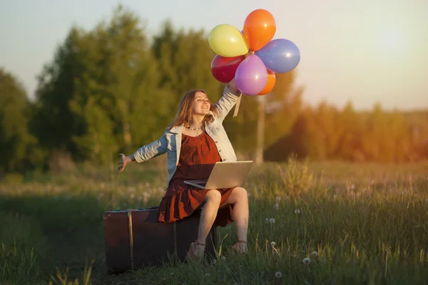 Feliz joven sentada en una gran maleta sosteniendo colorido ballo — Foto de Stock