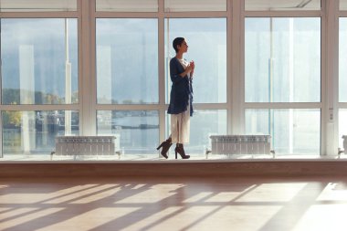 Büyük pencere duran ve denize bakarak kadın. Büyük pencere, cam duvar, deniz günbatımı.