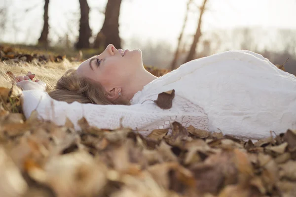 Chica disfrutando de cálidos días de otoño acostado en las hojas amarillentas — Foto de Stock