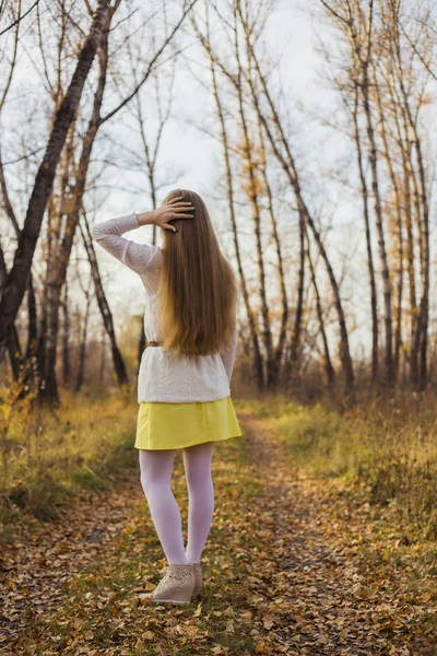La chica de blanco de pie en la carretera en el fondo del bosque de otoño — Foto de Stock