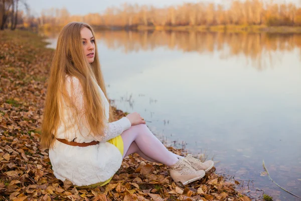 Zonnige herfstdag die een meisje met rode haren op de oevers van lake zit Stockfoto