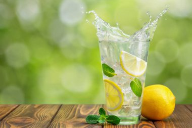 Ahşap masanın üzerinde yeşil bulanık arka planı olan bir limonata.