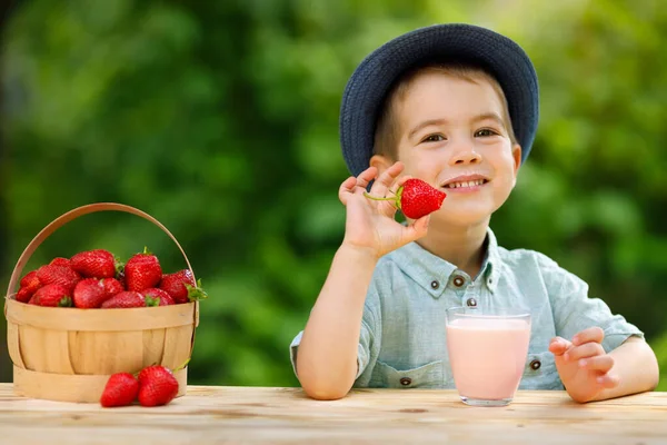 Little boy eats ripe strawberry and drinks yogurt from glass — Stock Photo, Image