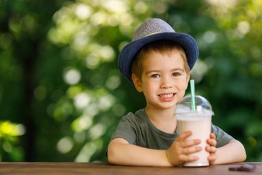 Küçük çocuk tek kullanımlık plastik bardak çikolatalı milkshake tutuyor.