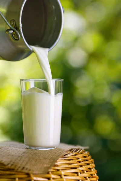 Milk pouring from metal can into glass — Stock Photo, Image