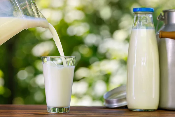 Mjölk som hälls från kanna i glas utomhus — Stockfoto