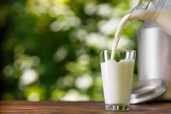 Milk pouring from jug into glass outdoors — Stock Photo, Image