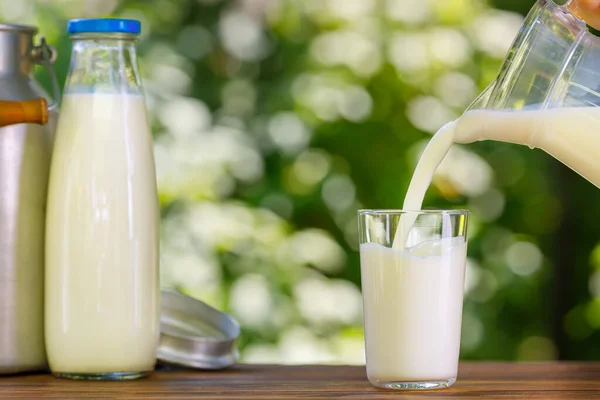 Mjölk som hälls från kanna i glas utomhus — Stockfoto