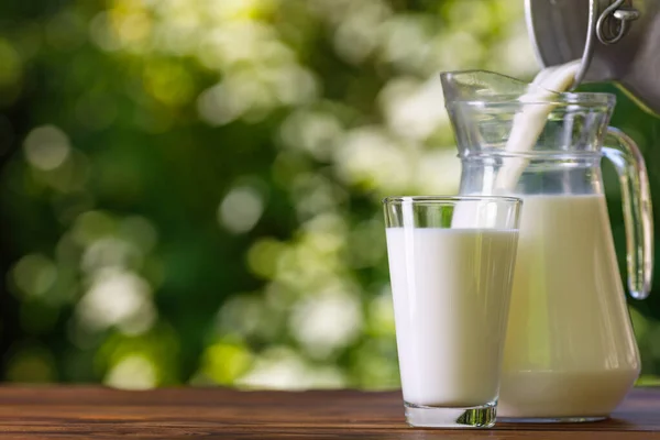 Melk die van een metalen kan in een glazen kan wordt gegoten buiten — Stockfoto