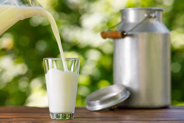 Milk pouring from jug into glass outdoors — Stock Photo, Image