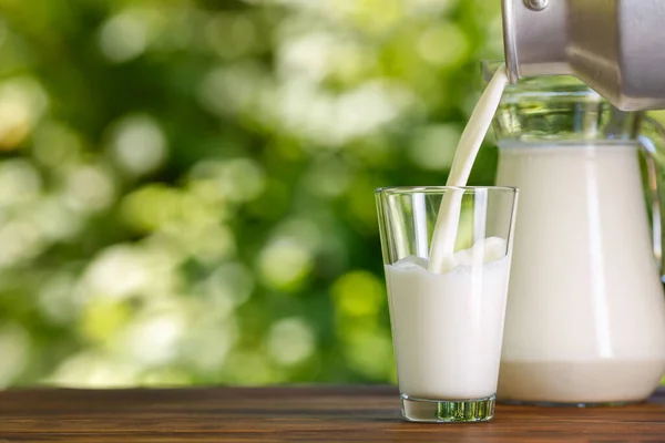 Milk pouring from metal can into glass outdoors — Stock Photo, Image