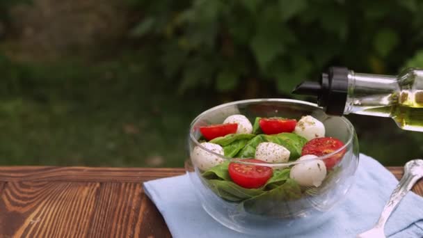 Olijfolie die uit de fles wordt gegoten in een glazen kom met verse salade — Stockvideo