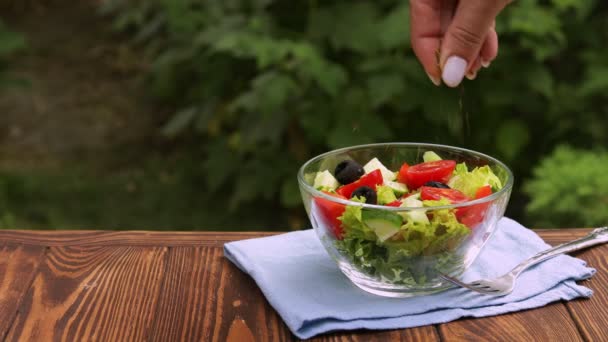 Mano femenina rociando especias en tazón de vidrio con ensalada fresca — Vídeo de stock