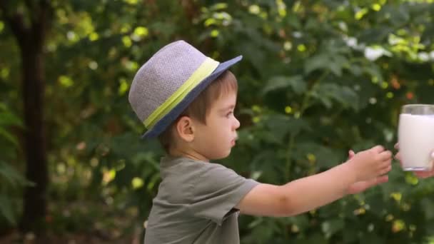 Liten pojke i hatt dricka mjölk utomhus — Stockvideo